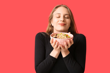Young woman with bowl of healthy oatmeal on red background