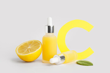Paper letter C, lemon and bottles of essential oil on grey background