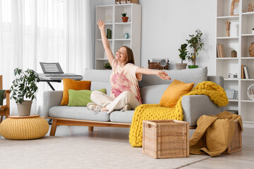 Happy young woman sitting on grey sofa in living room