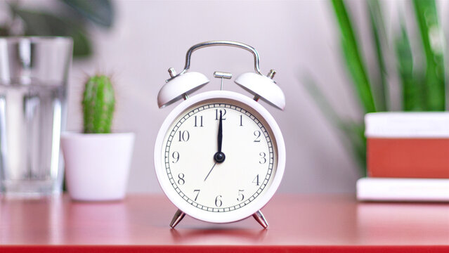 Classic white clock on a table. The clock hand points at 12:00, 00:00 close up photo interior