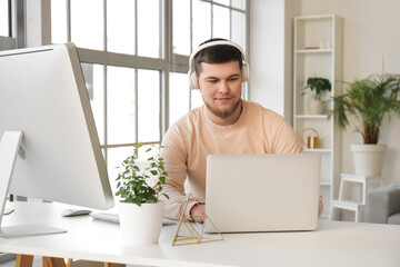Young bearded man in headphones using laptop on table at home