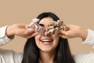 Happy woman with silk scrunchies on beige background