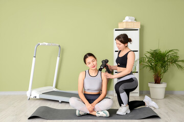 Female physiotherapist massaging young woman's shoulder with percussive massager on mat in...
