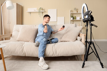 Male blogger with percussive massager and attachment recording video at home