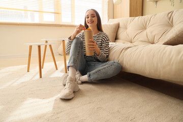 Young woman with potato chips sitting on floor at home