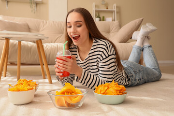Young woman with soda and bowls of chips lying on floor at home