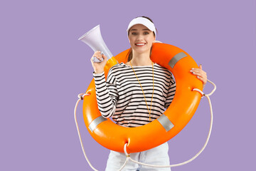 Young female lifeguard in cap with rescue ring and megaphone on lilac background
