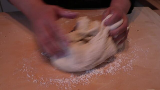 Woman kneading dough in flour on wooden table.
