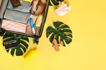 Suitcase with clothes, beach accessories, vibrator and palm leaves on color background