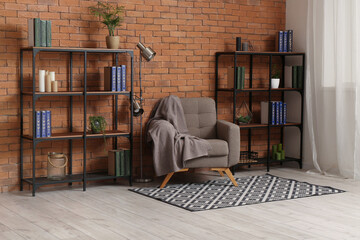Shelving units, grey armchair and lamp near brown brick wall in living room