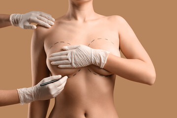 Plastic surgeon marking woman's breast on brown background, closeup