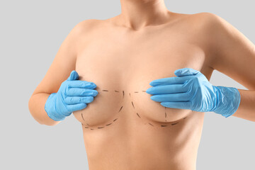 Naked young woman in medical gloves with marks on her breasts against light background, closeup. Plastic surgery concept