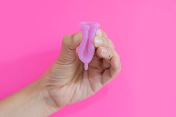 Close up of woman hand folding menstrual cup showing how to use, c form isolate on pink background.