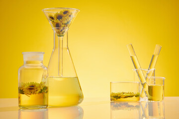 Yellow essence contained on most of lab glassware on white table against yellow background,...