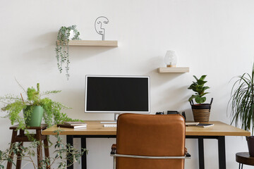 Modern workplace with computer monitor and houseplants near light wall in office