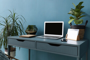 Modern workplace with laptop and houseplants near blue wall in office
