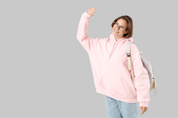 Happy female student with backpack waving hand on white background