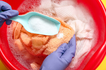 Woman in rubber gloves adding laundry detergent to clothes in plastic basin, closeup