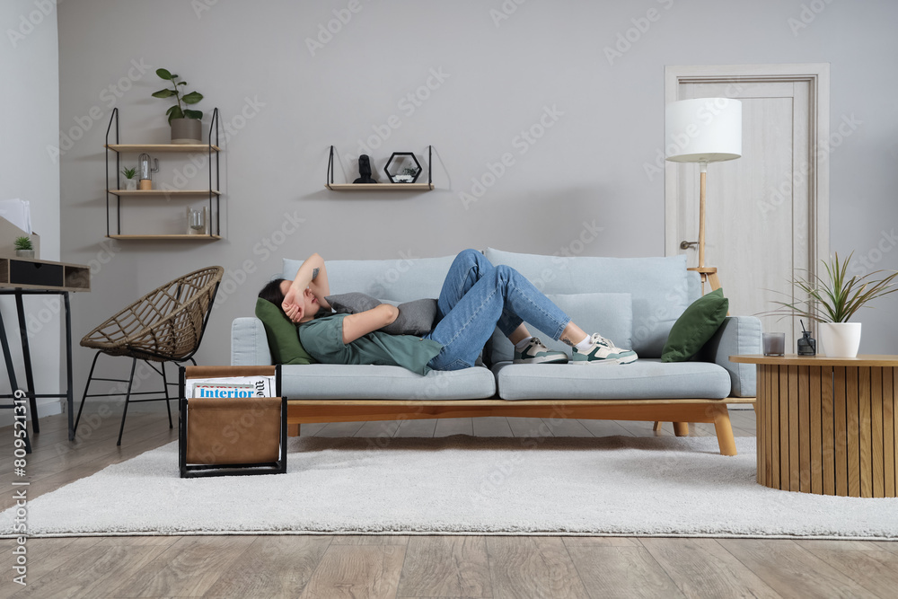 Sticker depressed young woman with pillow lying on sofa at home