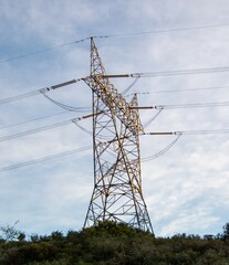 A large electricity pylon erected on a small hill in early morning sunlight image in vertical...