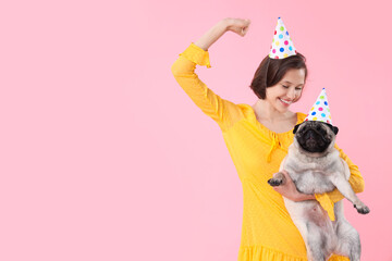 Young woman and cute pug dog in party hats on pink background