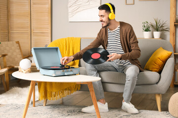 Young bearded man in headphones with record player listening to music at home