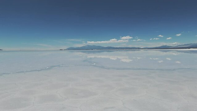 Drone flies over the water surface in the natural salt flat of Salinas Grande. Andean mountains on the horizon. Jujuy, Argentina. 4k.