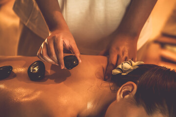 Naklejka premium Hot stone massage at spa salon in luxury resort with warm candle light, blissful woman customer enjoying spa basalt stone massage glide over body with soothing warmth. Quiescent