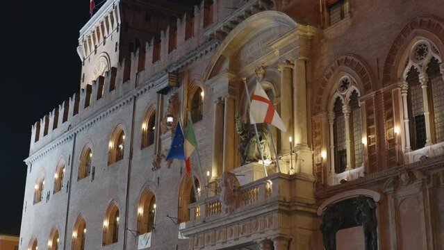 Bologna, Italy and EU flags waving on facade od Palazzo d Accursio at night with Statue of Pope Gregory XIII disguised as Saint Petronius