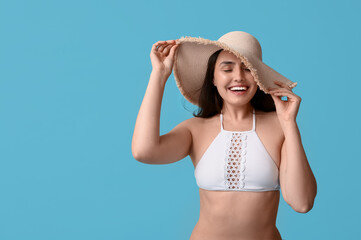 Beautiful young woman in swimsuit and hat on blue background