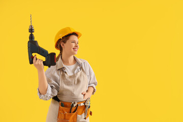 Young female carpenter with drill on yellow background. Labor Day celebration