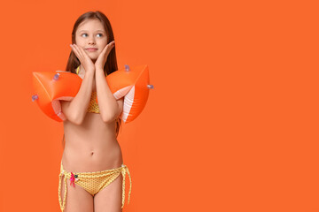 Cute little happy girl in swimsuit with inflatable armbands on orange background