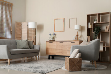 Interior of modern living room with wooden chest of drawers and comfortable armchairs near beige...