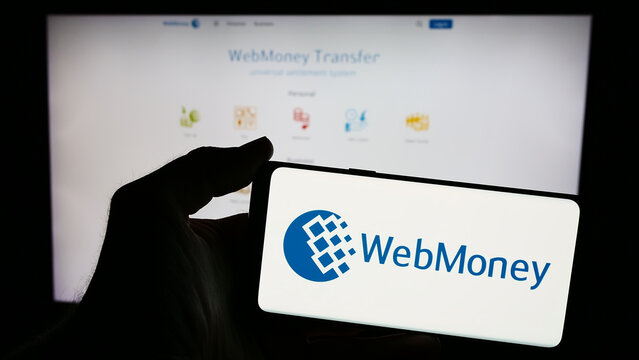 Stuttgart, Germany - 05-03-2024: Person holding mobile phone with logo of Russian online payment company WebMoney Transfer in front of business web page. Focus on phone display.