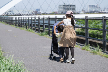 川沿いの河川敷でベビーカーを押す下の子の面倒を見るかわいい姉