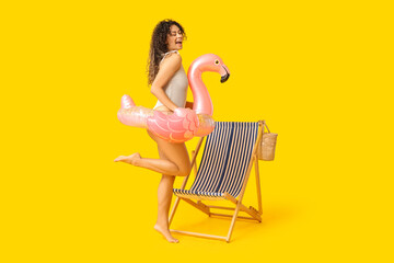 Beautiful young African-American woman with inflatable ring in shape of flamingo and deck chair on...