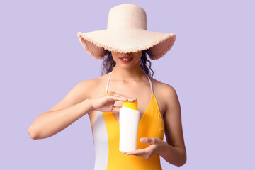 Beautiful young African-American woman in swimsuit and wicker hat with bottle of sunscreen cream on...