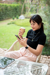 A woman sits at a table in a garden enjoying coffee and chatting with her friend on the phone.