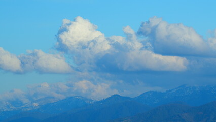 Snow-Capped Rocky Mountains With Blue Sky And Opposite Direction Clouds.