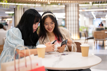 Two happy young Asian female friends are hanging out together at the shopping mall on the weekend.