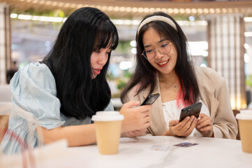Two happy young Asian female friends are hanging out together at the shopping mall on the weekend.