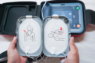 Automatic external defibrillator. Portable defibrillator on a wooden table. Defibrillator for medical care. Device for provision of emergency medical care. Automatic cardioverter with nursing manual