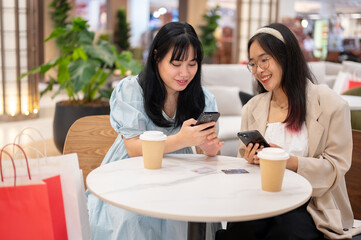 Two Asian female friends are relaxing in a cafe in the shopping mall after shopping together.
