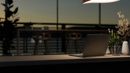 A laptop computer on a wooden desk under dim light in a contemporary dark co-working space at night.