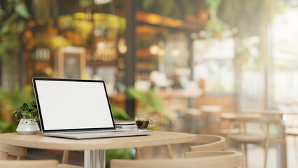 A laptop computer mockup and a coffee cup on a wooden table in a beautiful contemporary coffee shop.