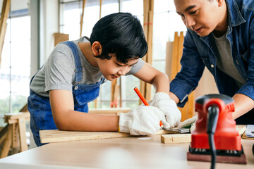 Happy Asian father and son carpentry wearing safety gloves. Father teaches his son to measure wood...