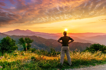 rejoicing man with beautiful scenic mountain sunset landscape on background. happy man watching...