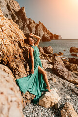 Woman green dress sea. Woman in a long mint dress posing on a beach with rocks on sunny day. Girl...