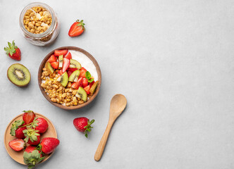 Natural yogurt with granola, kiwi and strawberries in a wooden bowl on a light background with...