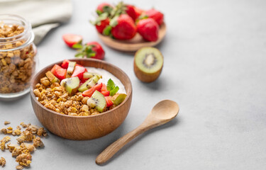 Natural yogurt with granola, kiwi and strawberries in a wooden bowl on a light background with...